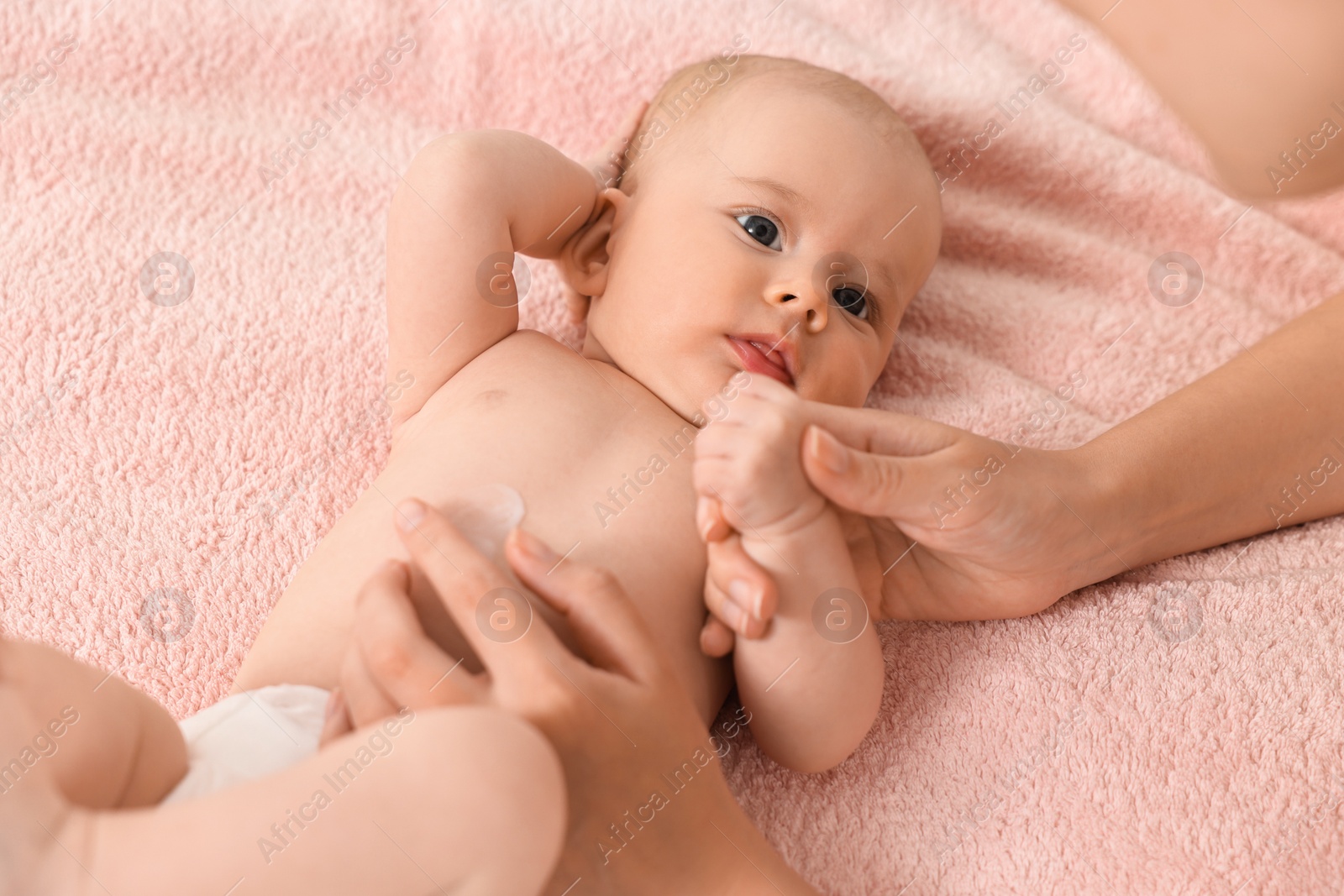 Photo of Woman applying body cream onto baby`s skin on bed, closeup