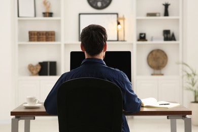 Photo of Home workplace. Man working at wooden desk in room, back view