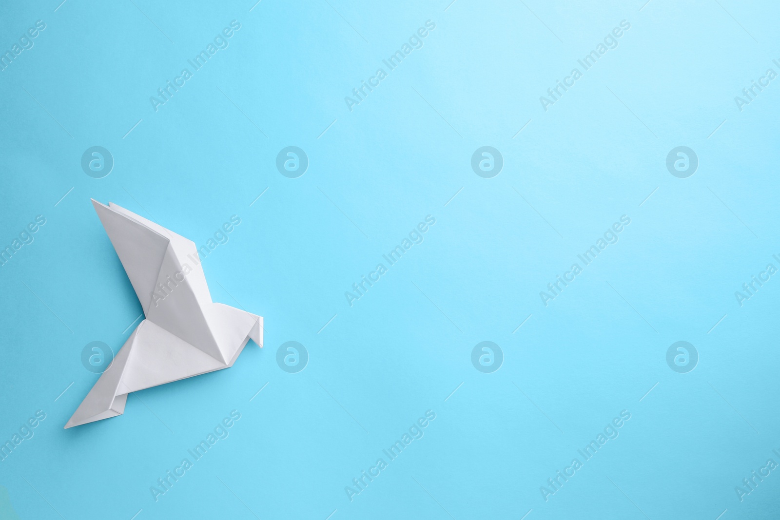 Photo of Origami art. Beautiful handmade paper bird on light blue background, top view. Space for text