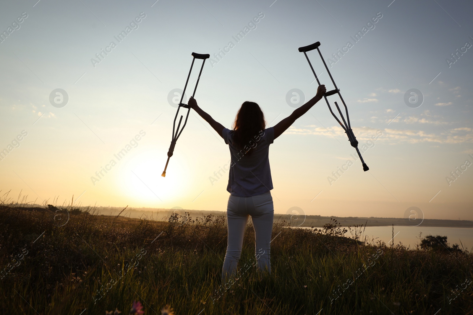 Photo of Woman holding axillary crutches outdoors at sunrise, back view. Healing miracle