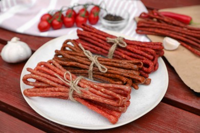 Photo of Bundles of delicious kabanosy with garlic and tomatoes on wooden table