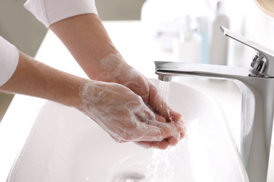 Man washing hands with soap over sink in bathroom, closeup