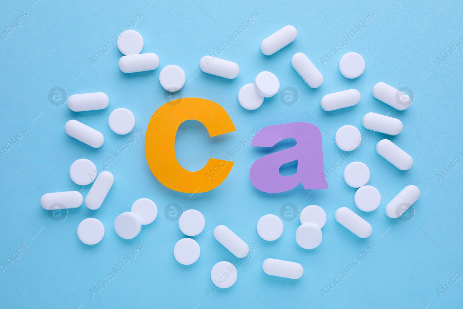 Photo of Calcium symbol made of colorful letters and white pills on light blue background, flat lay