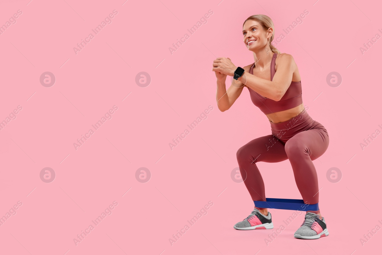 Photo of Woman exercising with elastic resistance band on pink background, low angle view. Space for text