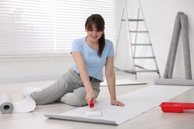 Woman applying glue onto wallpaper sheet in room