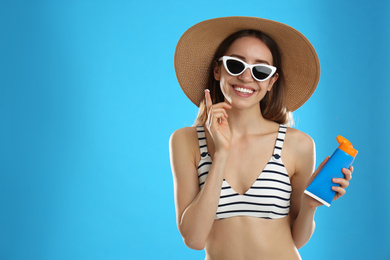 Photo of Young woman applying sun protection cream on light blue background. Space for text