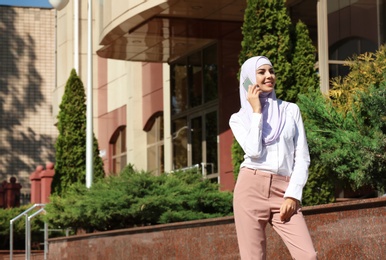 Photo of Muslim woman in hijab talking on phone outdoors