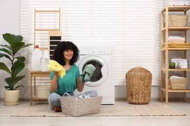 Happy woman with laundry near washing machine indoors