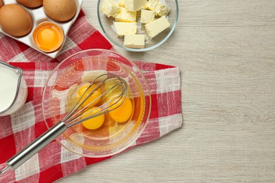 Photo of Whisk, eggs in bowl, milk and butter on white wooden table, flat lay. Space for text