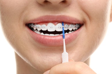 Photo of Woman with dental braces cleaning teeth using interdental brush on white background, closeup