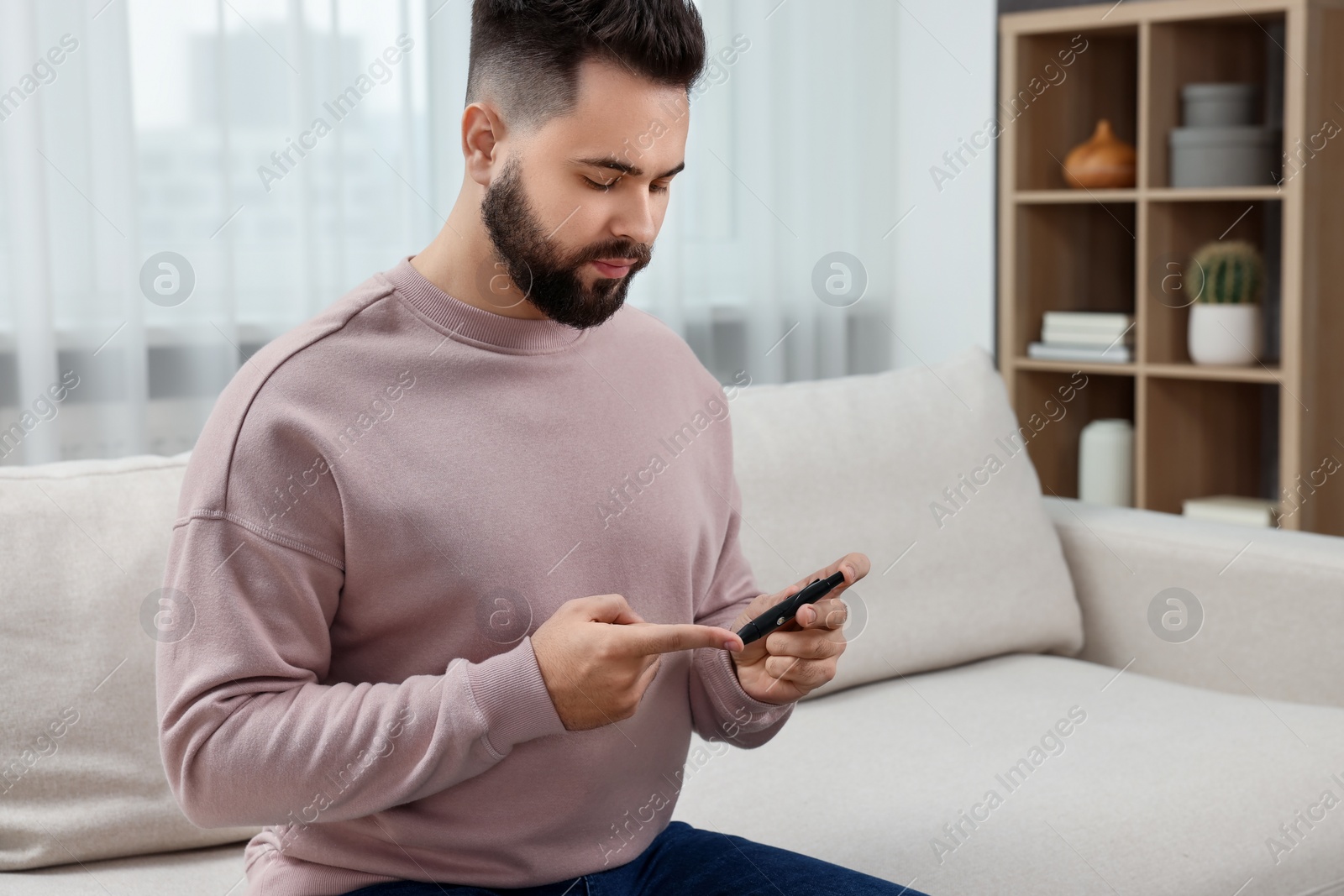 Photo of Diabetes test. Man checking blood sugar level with lancet pen on sofa at home