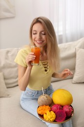 Photo of Young woman with glass of juice and exotic fruits indoors
