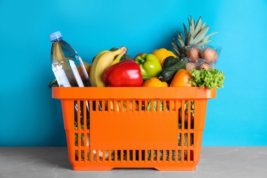 Photo of Shopping basket with grocery products on grey table against light blue background