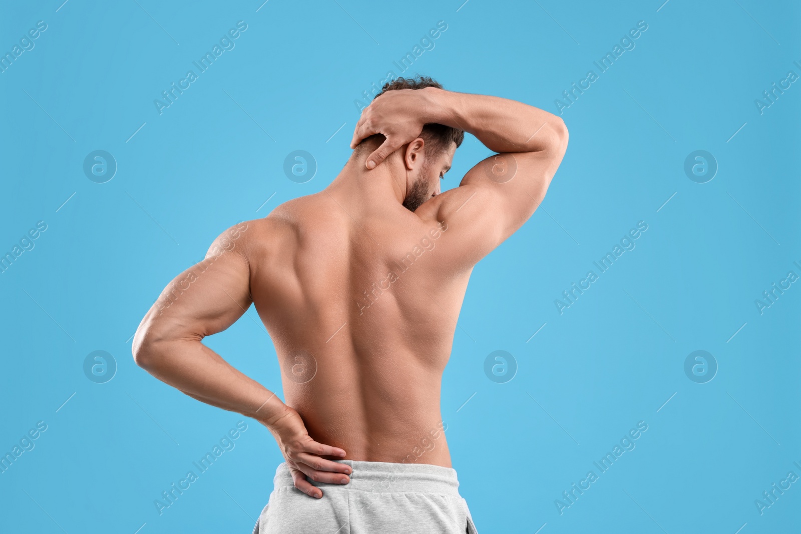 Photo of Man suffering from back pain on light blue background, back view. Space for text