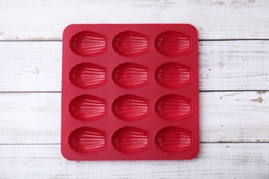 Photo of Red baking mold for madeleine cookies on white wooden table, top view