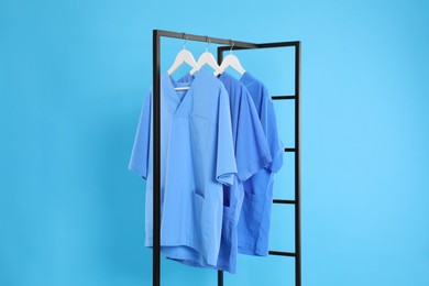 Photo of Medical uniforms on metal rack against light blue background