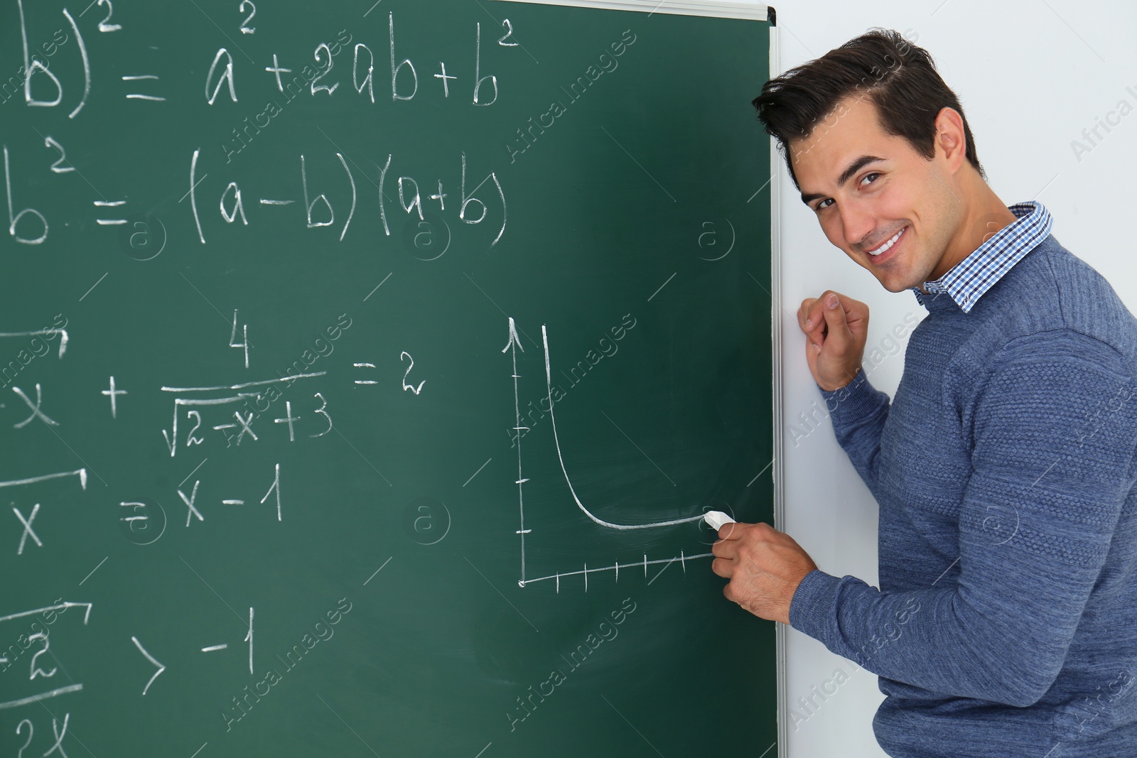 Photo of Young teacher drawing graph on chalkboard in classroom