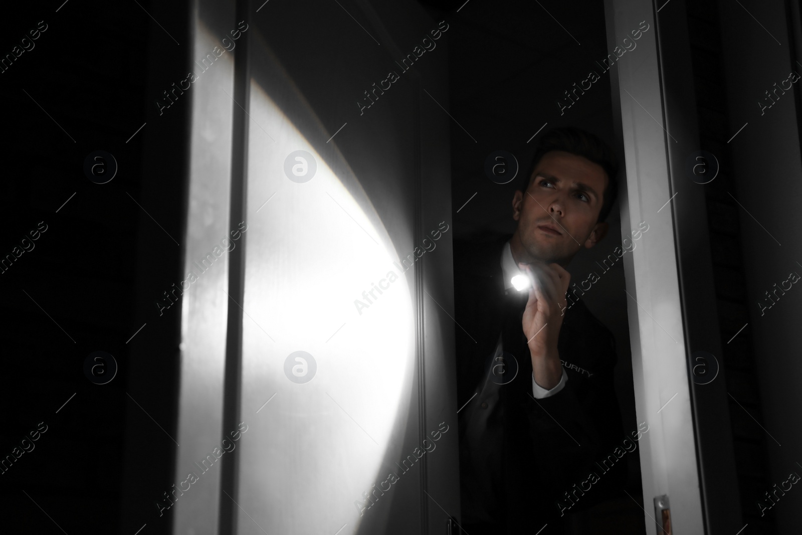 Photo of Male security guard with flashlight in dark room