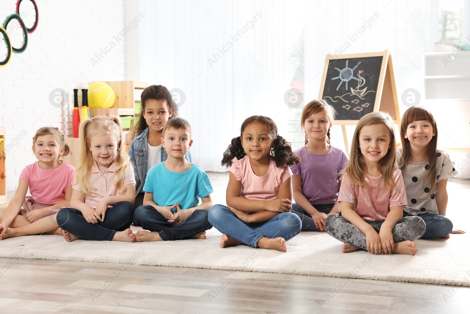 Photo of Group of cute little children sitting on floor indoors. Kindergarten playtime activities