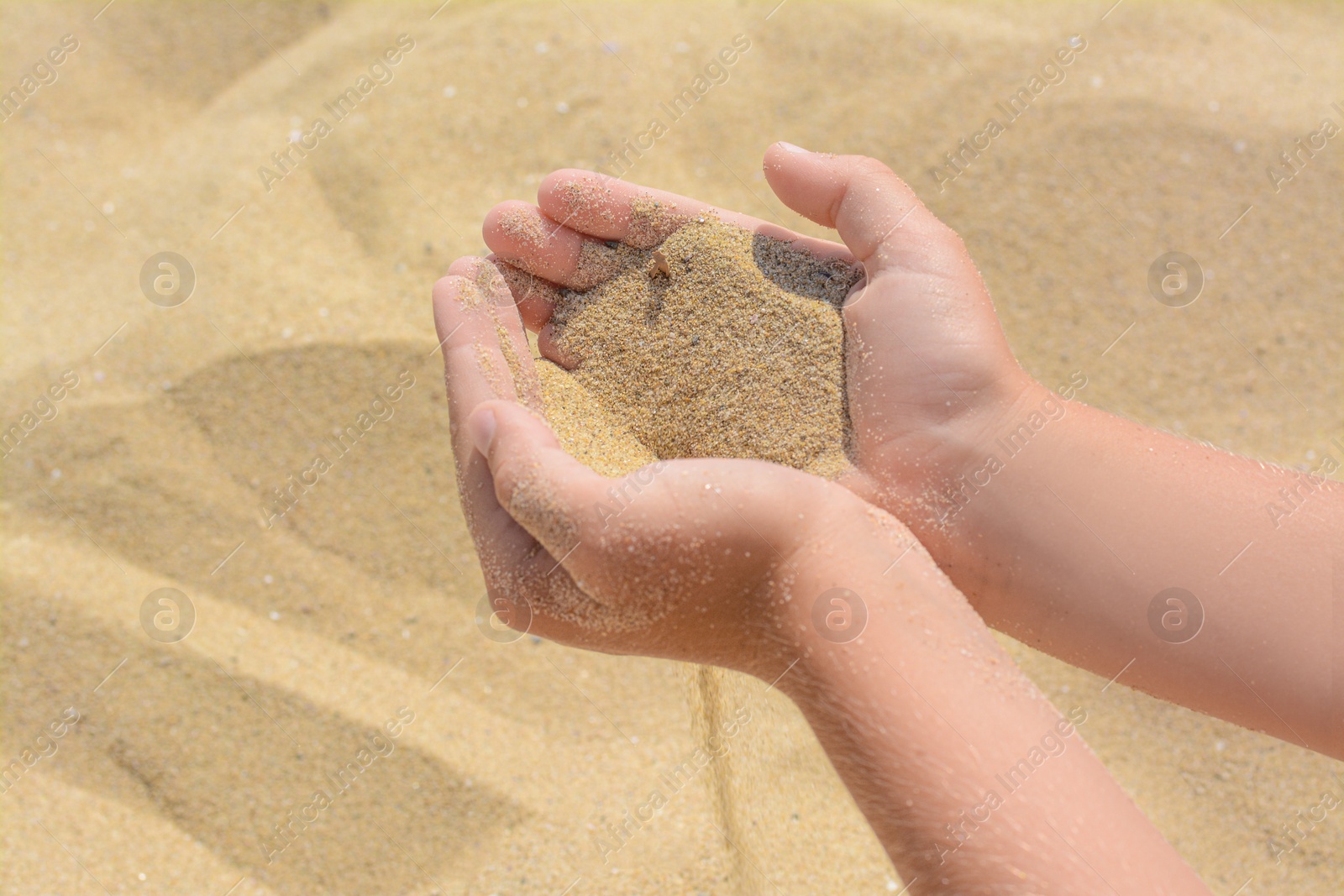 Photo of Child pouring sand from hands on beach, closeup. Fleeting time concept