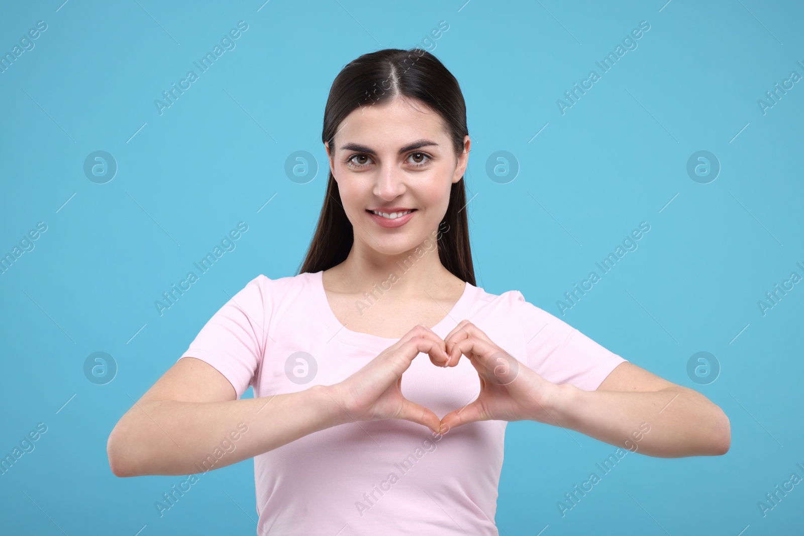 Photo of Beautiful young woman making heart with hands on light blue background