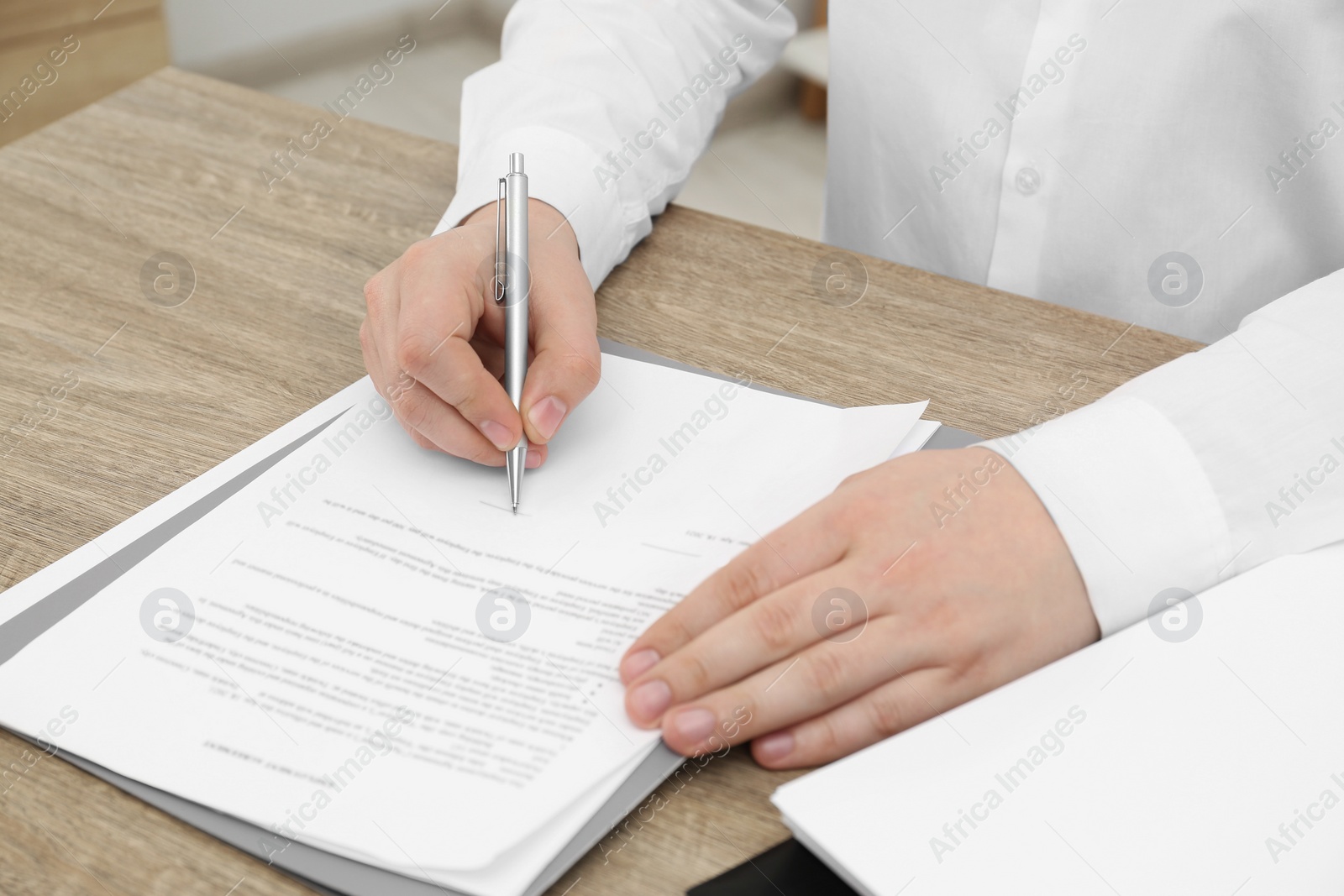 Photo of Man signing document at wooden table, closeup