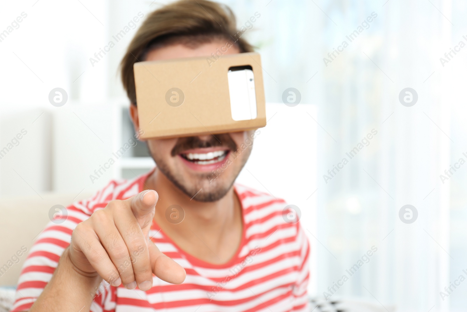 Photo of Young man using cardboard virtual reality headset at home