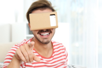 Photo of Young man using cardboard virtual reality headset at home