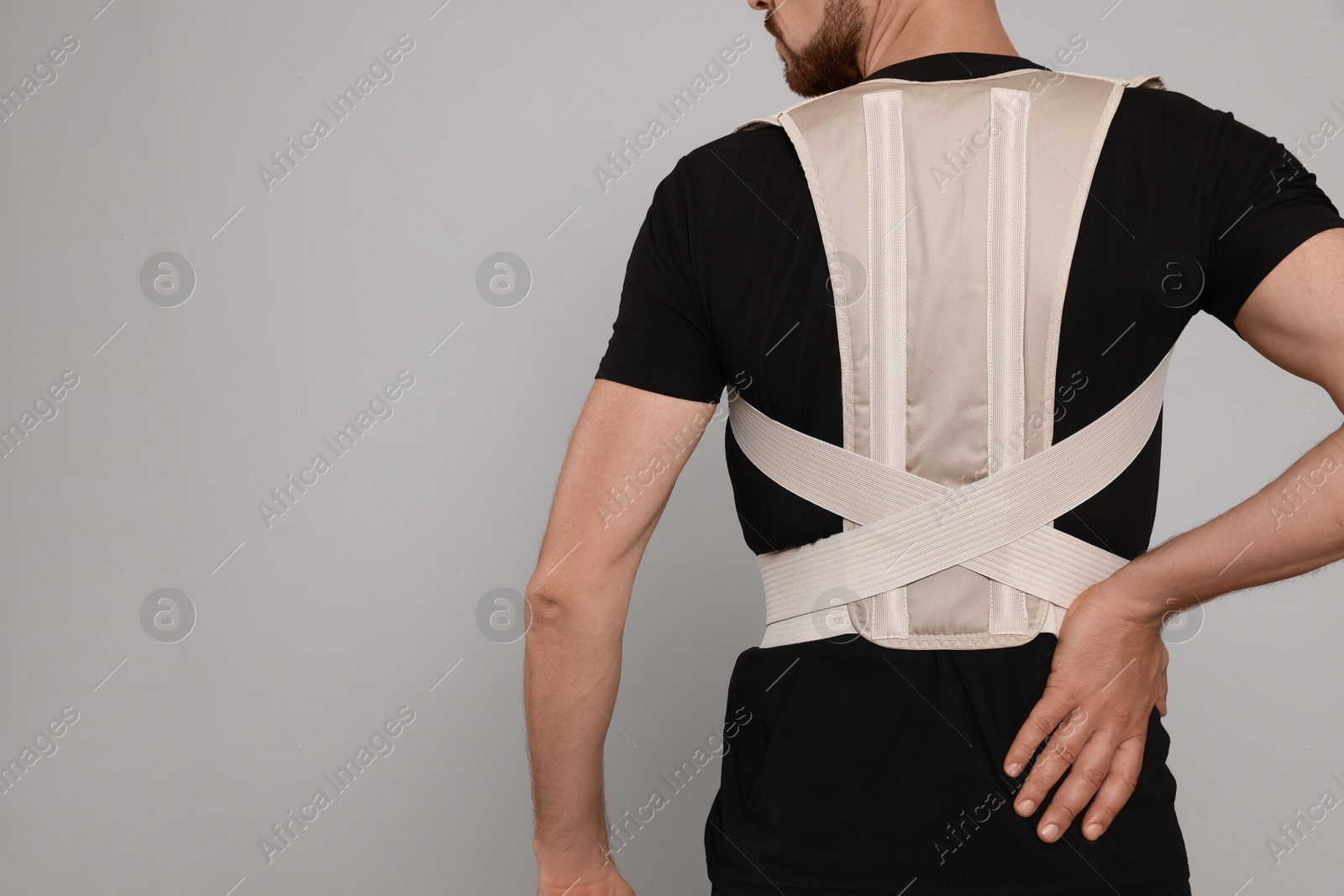 Photo of Closeup of man with orthopedic corset on grey background, back view. Space for text