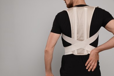 Closeup of man with orthopedic corset on grey background, back view. Space for text