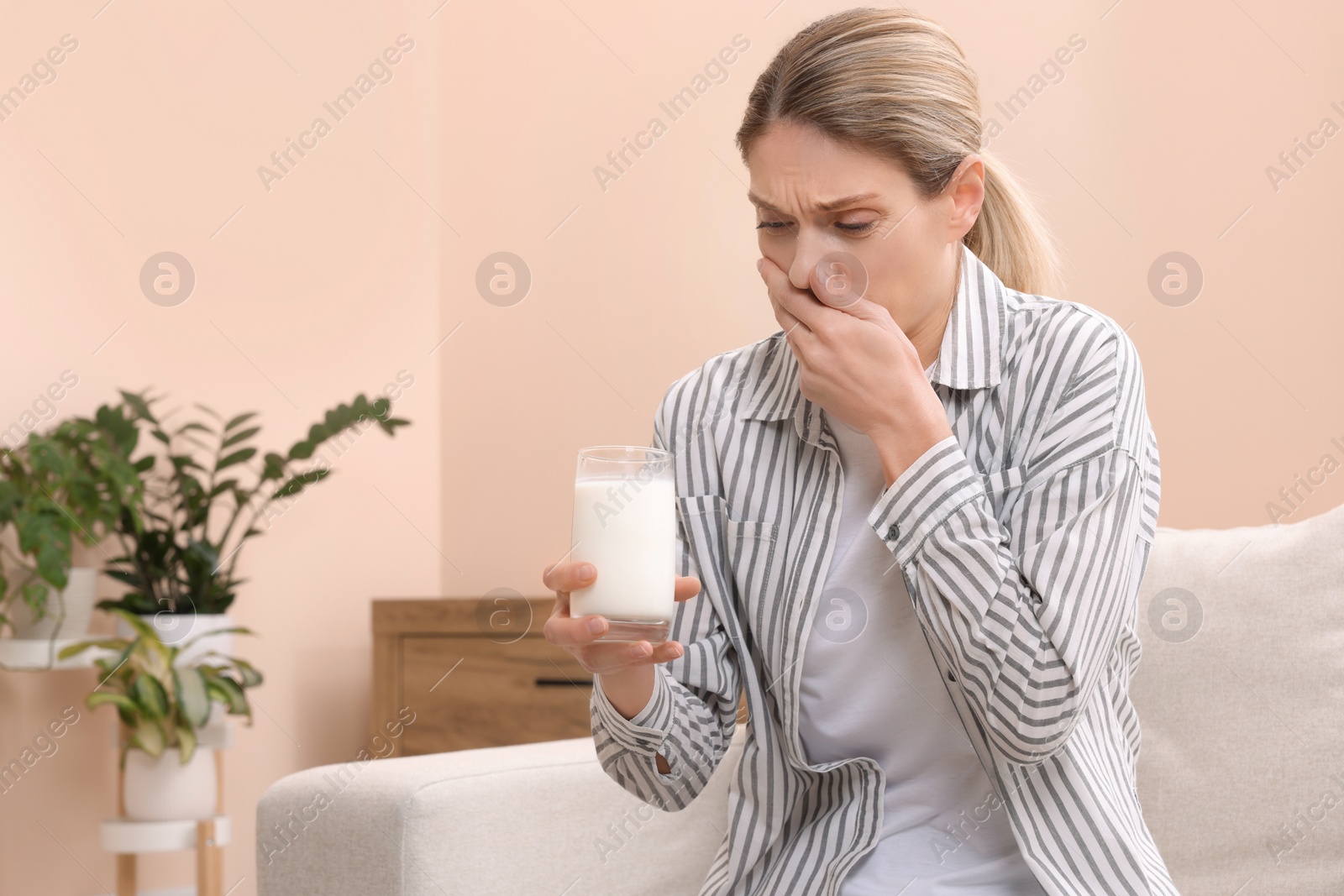 Photo of Woman with glass of milk suffering from lactose intolerance at home, space for text