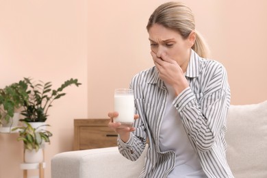 Woman with glass of milk suffering from lactose intolerance at home, space for text