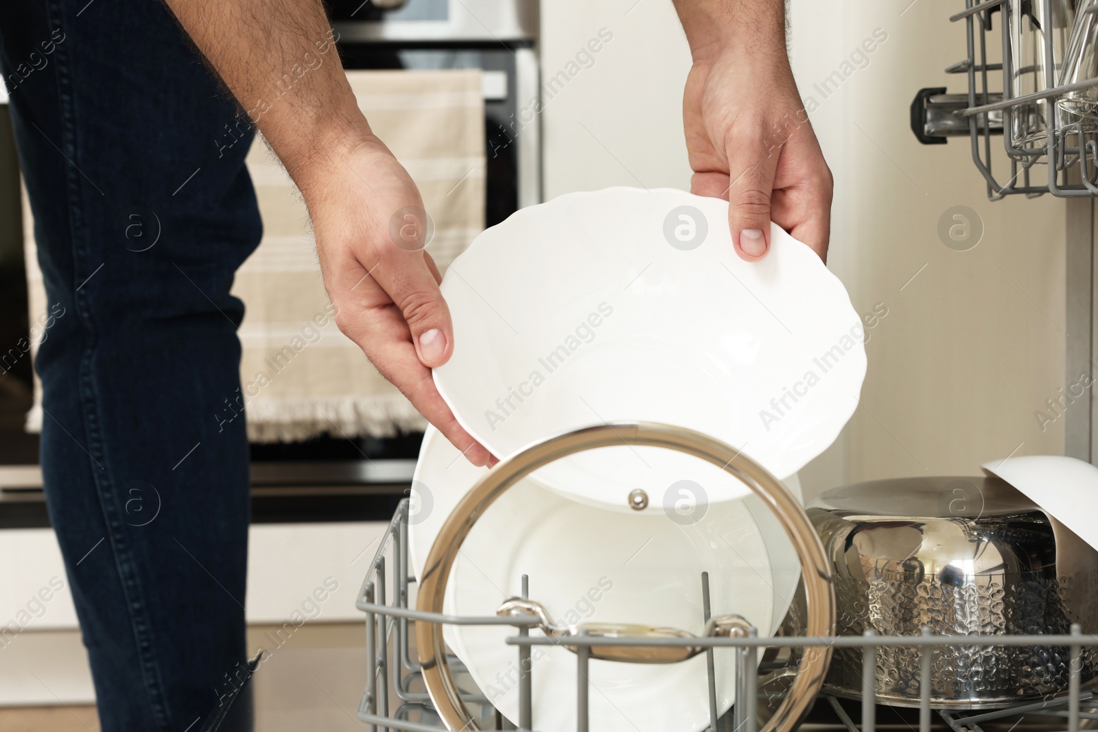 Photo of Man loading dishwasher with plates indoors, closeup