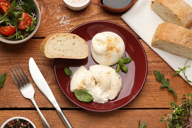 Photo of Delicious burrata cheese with arugula and fresh bread on wooden table, flat lay