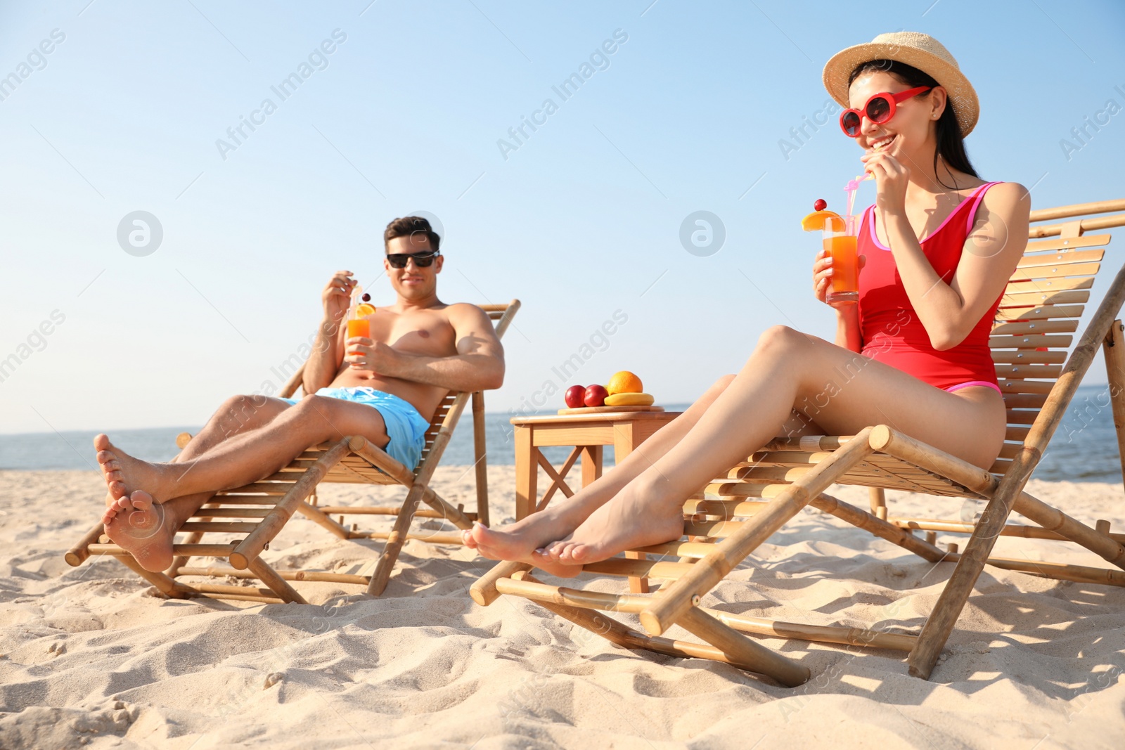 Photo of Couple with drinks resting on sunny beach at resort