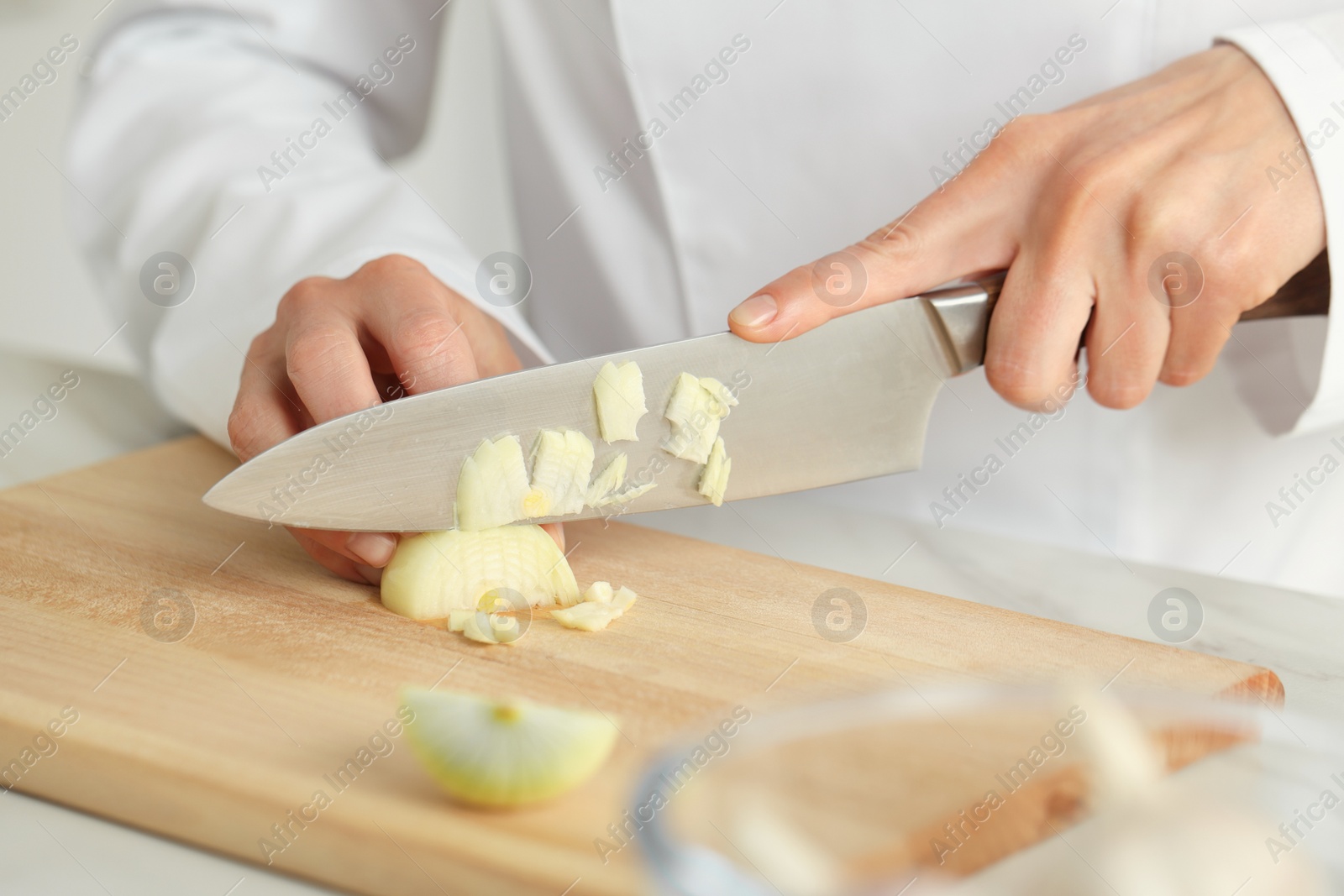 Photo of Professional chef cutting onion at white marble table indoors, closeup