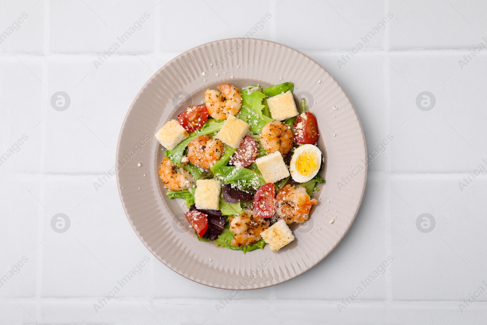 Photo of Delicious Caesar salad with shrimps on white tiled table, top view