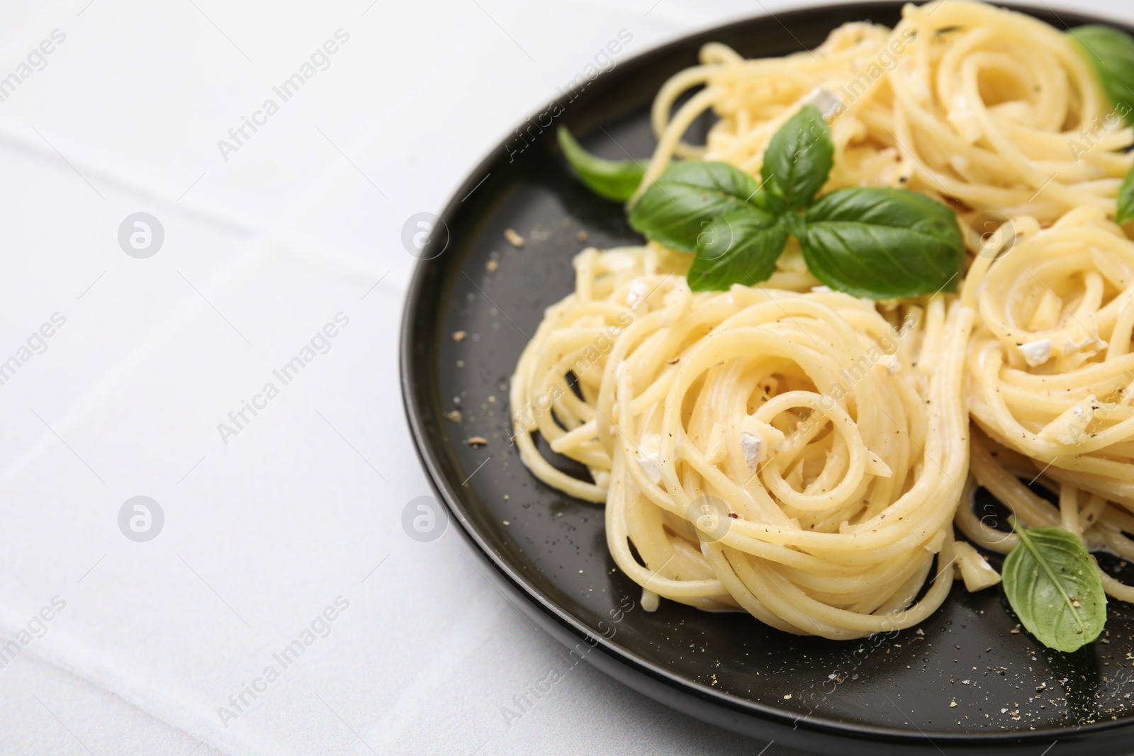 Photo of Delicious pasta with brie cheese and basil leaves on white tiled table, closeup. Space for text