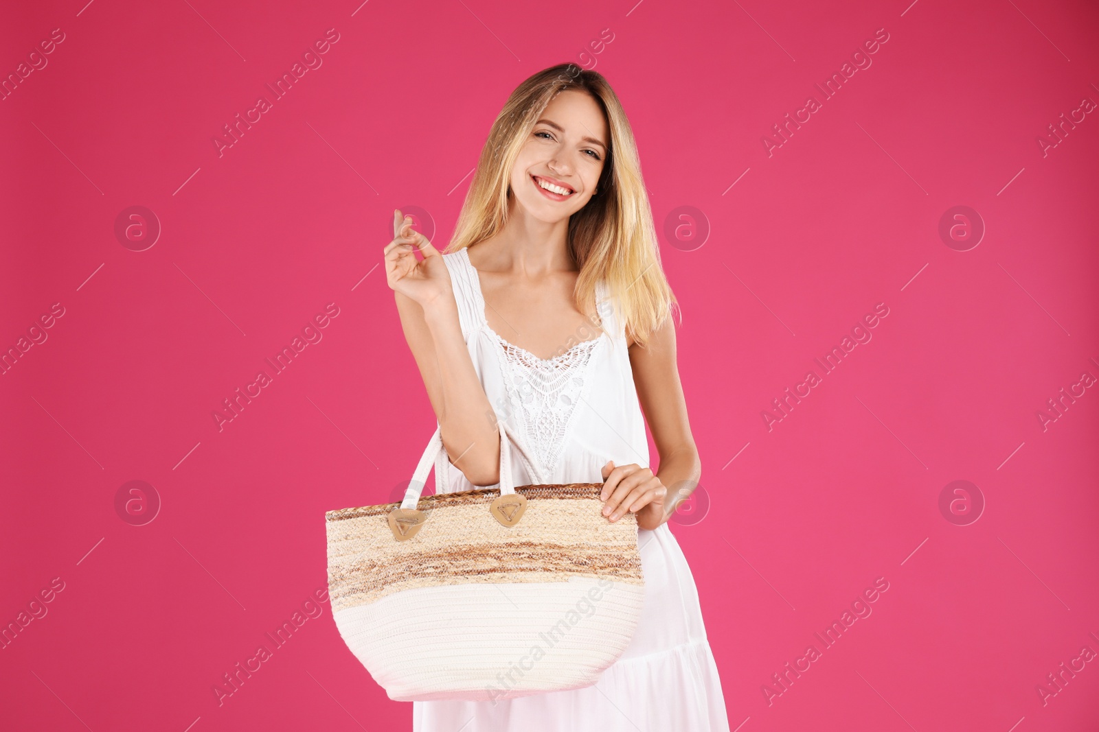 Photo of Beautiful young woman with stylish straw bag on pink background