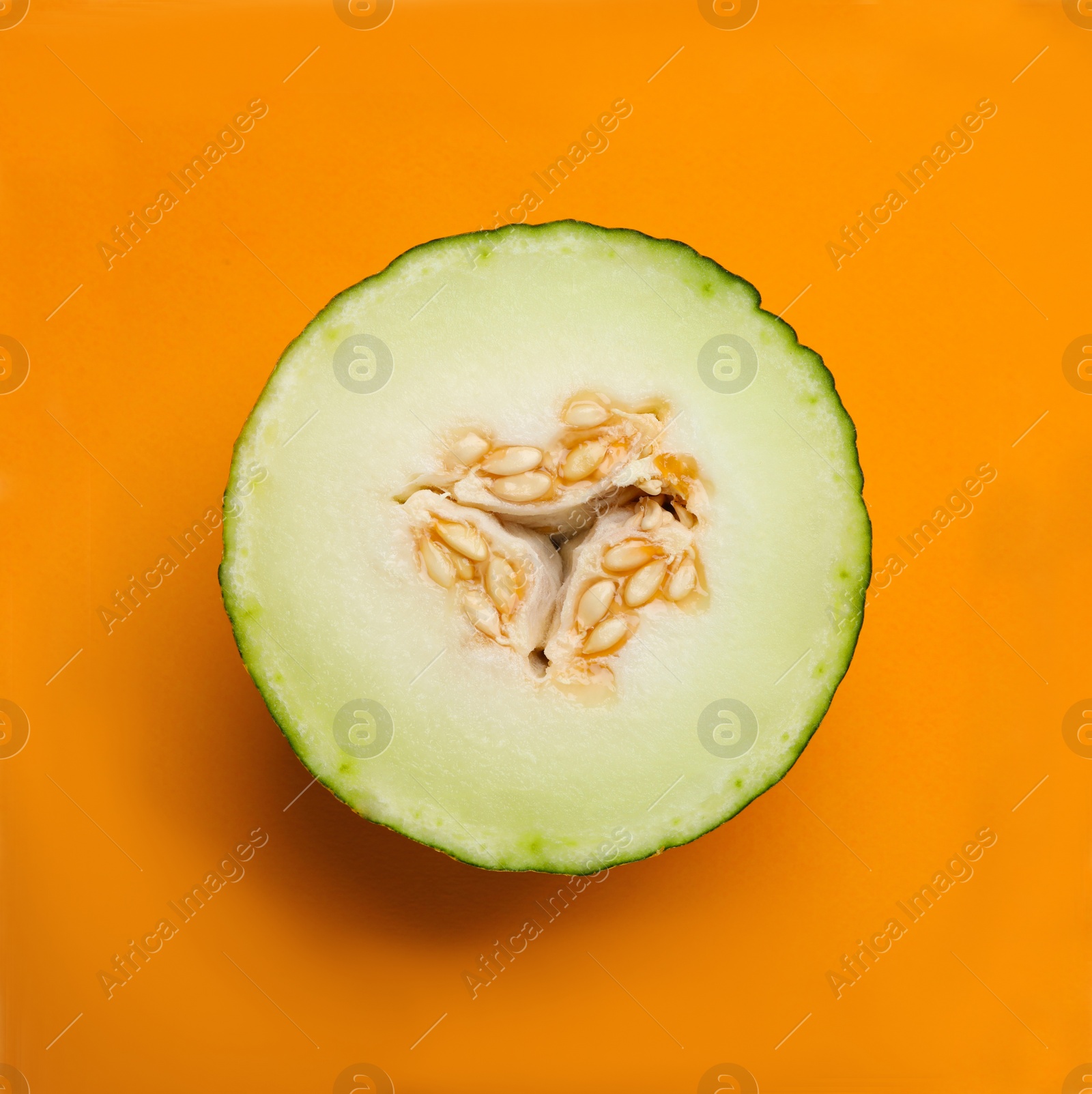 Photo of Half of ripe tasty melon on orange background, top view