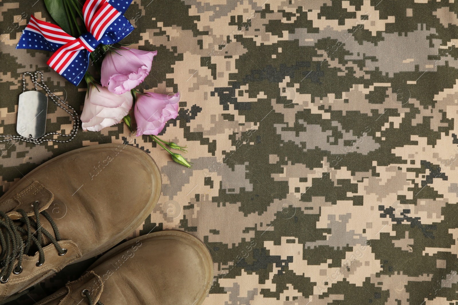 Photo of Flat lay composition with military boots and flowers on camouflage background, space for text. Armed Forces Day