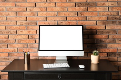 Modern computer monitor on desk against brick wall, mock up with space for text