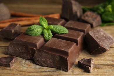 Photo of Tasty chocolate pieces and mint on wooden table, closeup