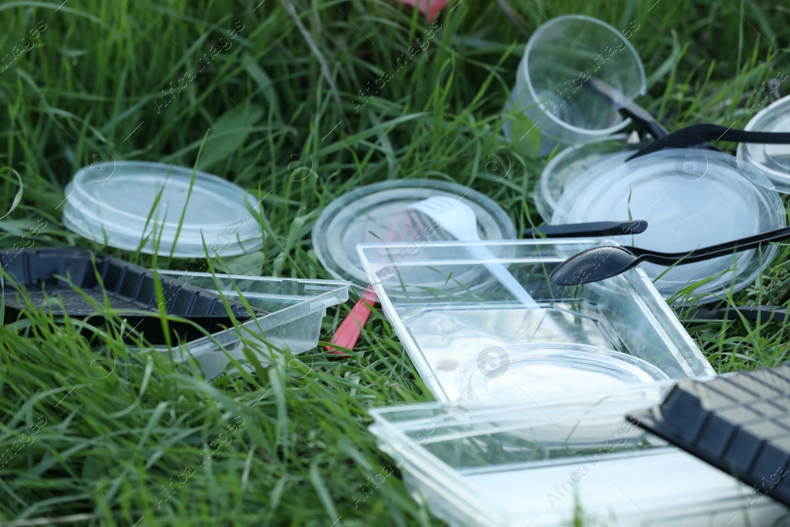 Photo of Used plastic tableware on grass outdoors, closeup. Environmental pollution concept