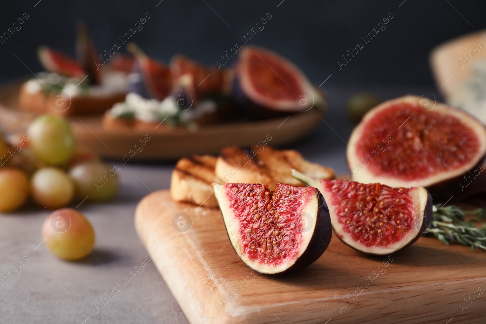 Photo of Wooden board with ripe fig slices on grey table, closeup