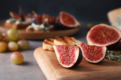 Wooden board with ripe fig slices on grey table, closeup