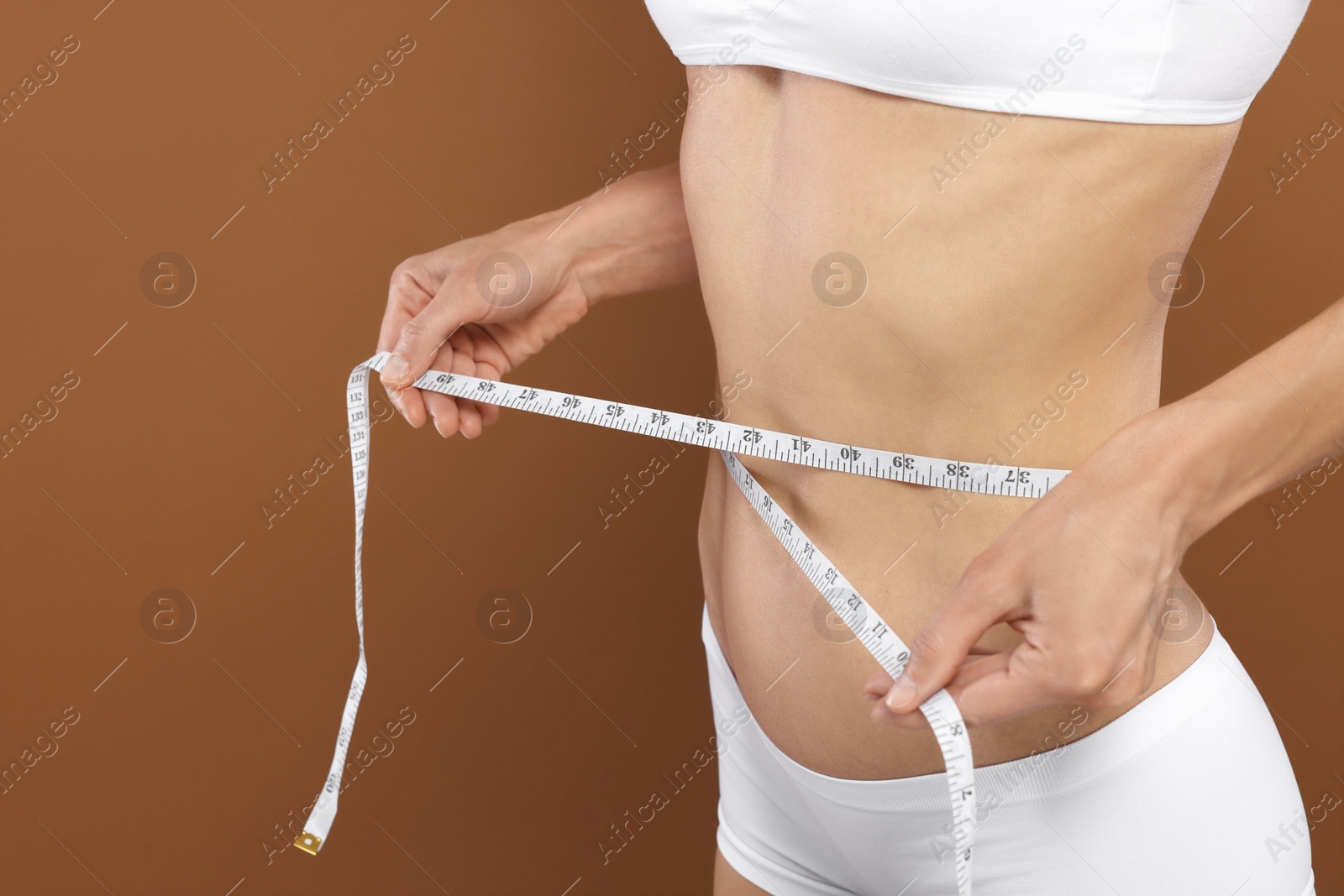 Photo of Slim woman measuring waist with tape on brown background, closeup and space for text. Weight loss