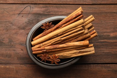 Bowl with cinnamon sticks and star anise on wooden table, top view