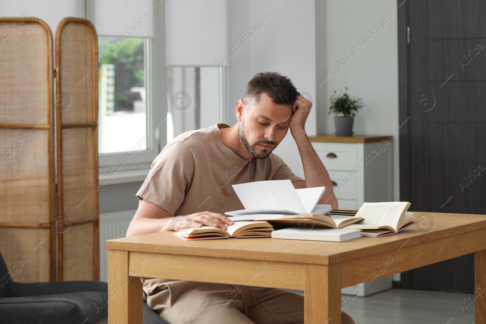 Photo of Sleepy man studying at wooden table indoors