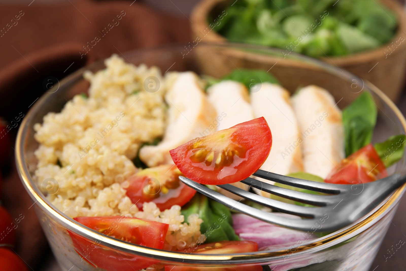 Photo of Fork with cherry tomato over bowl of delicious quinoa salad, closeup